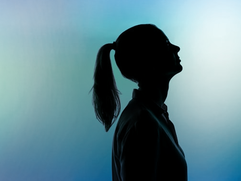 A dark silhouette of a woman from the side with a ponytail against a light blue-green gradient